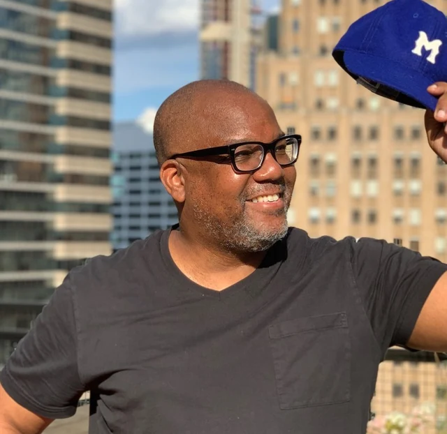 Kahlil (KB) Byrd outdoors, holding up a blue cap